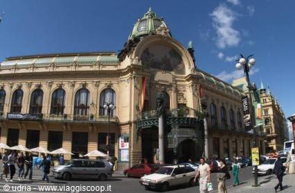 Municipal House in Prague: Art Nouveau facade with green dome, cars and pedestrians in sunshine