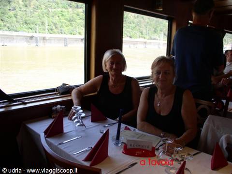 Two smiling women at a set table on a boat, river through the windows