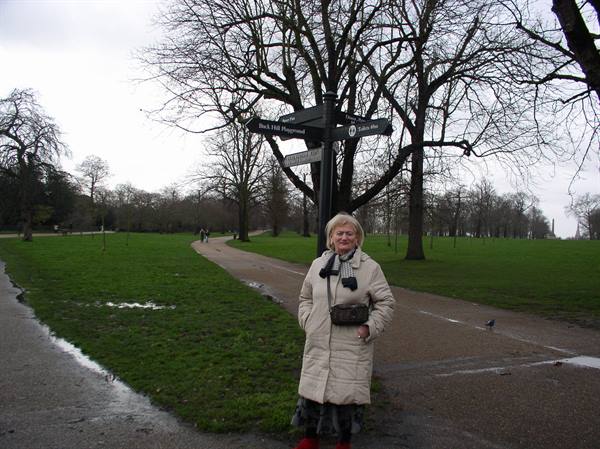 Woman in light coat beneath the Hyde Park signposts, bare winter trees