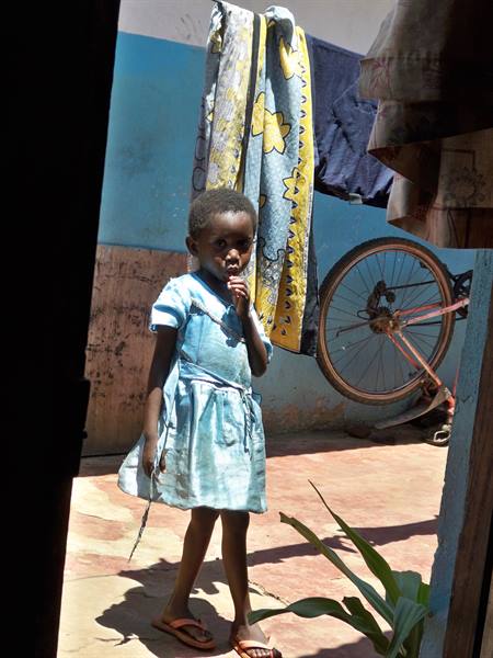 Girl in blue dress near a bicycle and hanging laundry in a courtyard