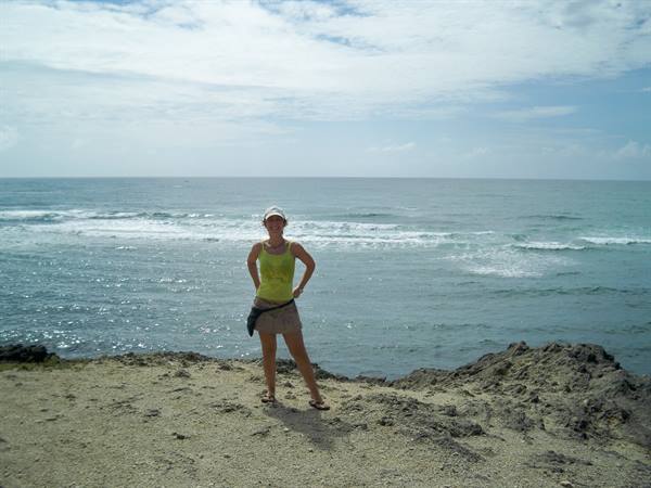 Woman in white cap posing on sandy rocks before waves