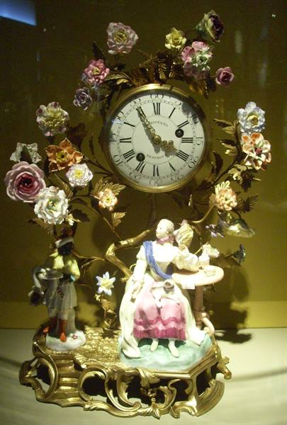 Gilded clock with porcelain flowers and figurines in a display case