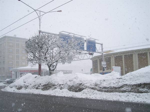 Snowfall over a city intersection, frosted tree and road signs, snow piles