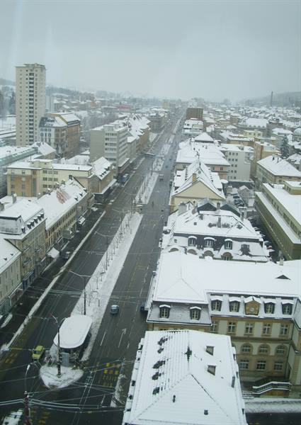 Snowy city seen from above, white rooftops and empty street