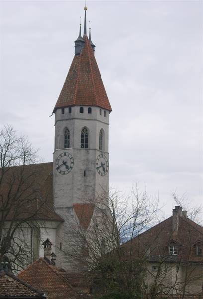 White church tower with clock and red roof, bare trees, grey sky