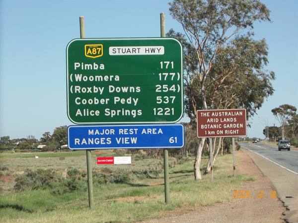 Green Stuart Highway distance sign to Alice Springs, Australian roadside under clear sky