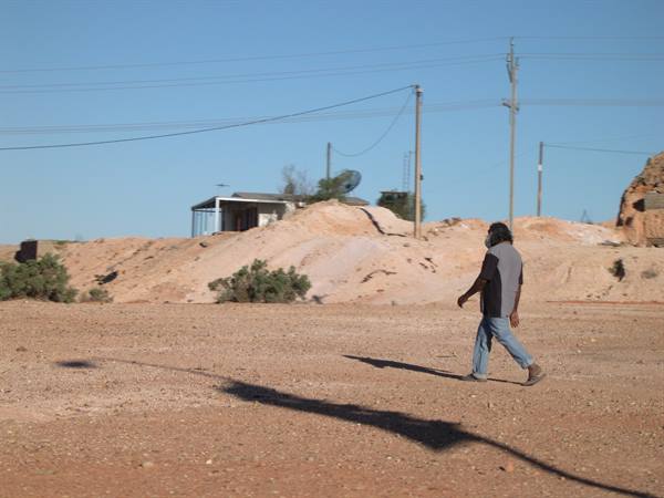 Man walks across red sand past opal mining mounds, Coober Pedy
