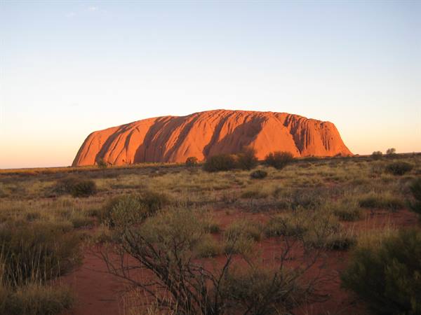 Uluru glowing red at dusk, dry scrub and ochre sand