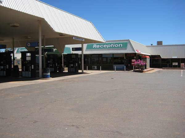 Roadhouse service station with fuel pumps and green Reception sign under blue sky