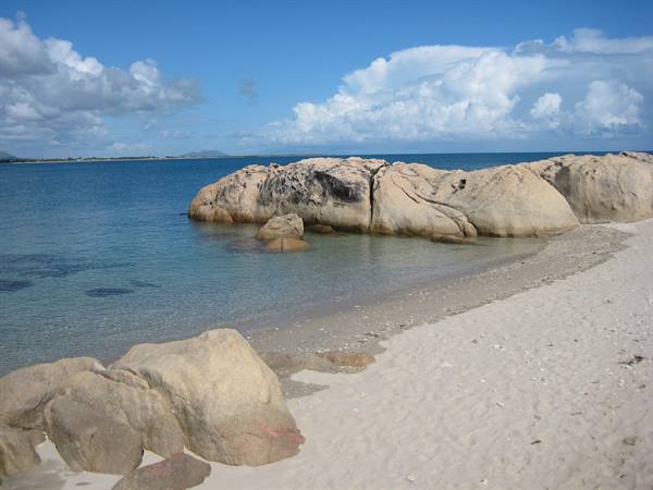 Large granite rocks on white sand, turquoise water and cloudy sky