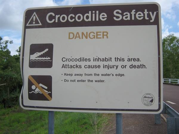 White warning sign cautions crocodile danger beside road guardrail
