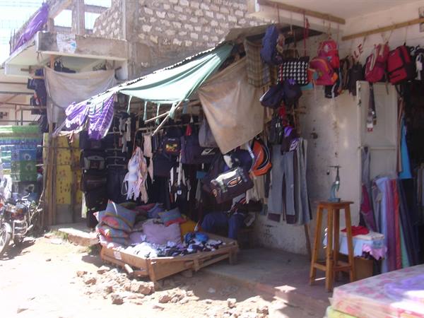 Street stall with hanging backpacks, clothes and green tarps under bright sunlight