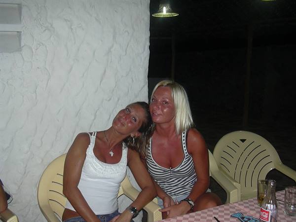 Two smiling women on plastic chairs by white wall, night