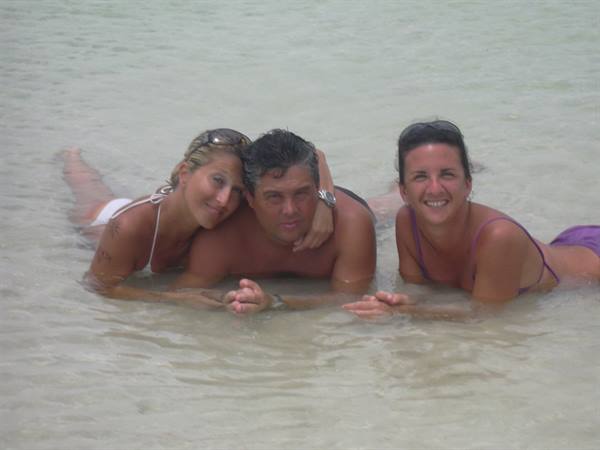 Three friends lying in shallow clear water on a sandy beach