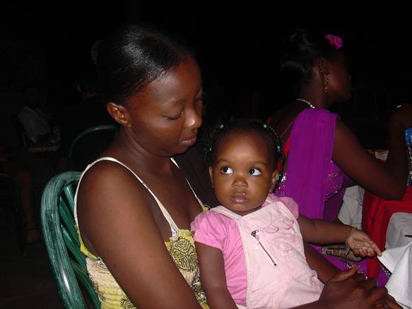 Woman and toddler sit on green plastic chairs at a dark indoor party