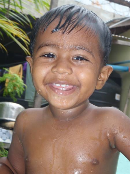 Smiling shirtless child, wet with water, in a courtyard with palm trees