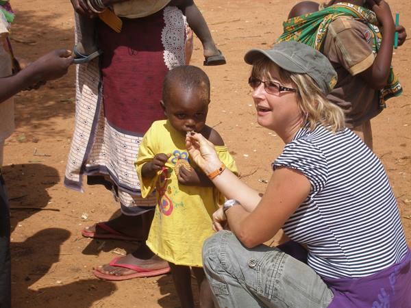 Crouching tourist feeds a child on red dirt among African women