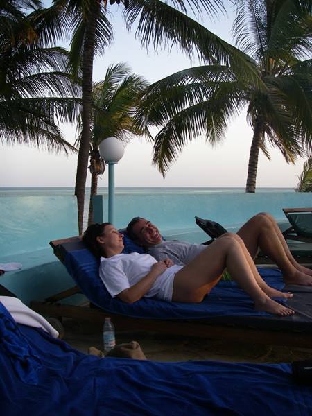 Couple laughing on sun loungers by pool among palms and ocean