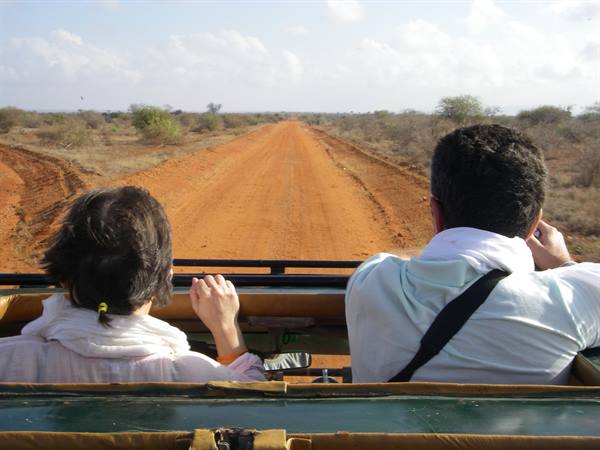 Two tourists in an open jeep on the red dirt savanna road