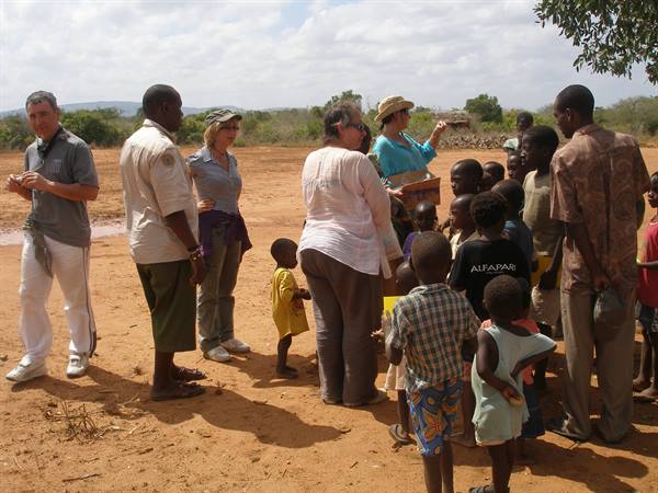 Tourists and children gather on red soil, a woman hands out food