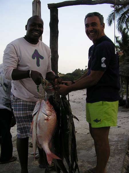 Two smiling men holding fresh caught fish on a beach