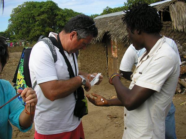 Tourist with backpack hands medicine to a man in front of thatched huts