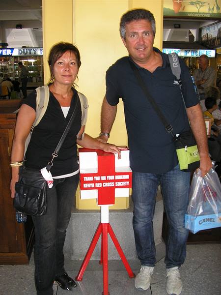 Couple with backpacks beside a Kenya Red Cross donation box at duty free