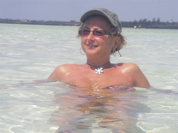 Woman in cap and sunglasses chest-deep in clear shallow turquoise sea