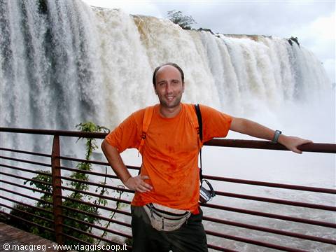Tourist in orange shirt in front of Iguazú Falls, near the railing
