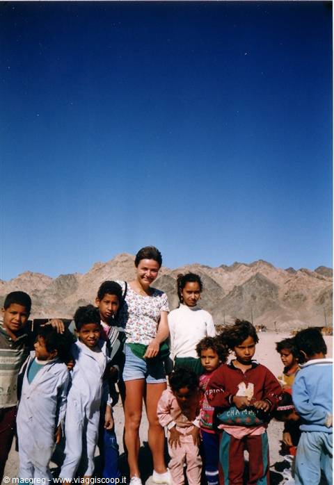 Smiling tourist with local children in the desert, rocky mountains behind