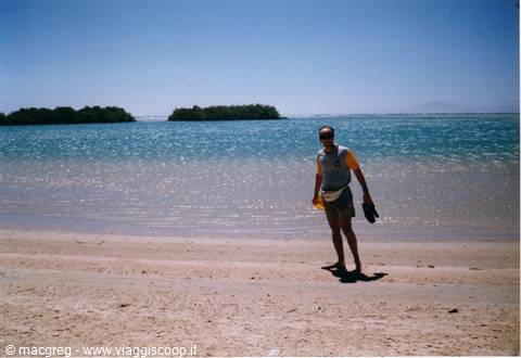 Man in yellow shirt walks on sand before turquoise sea and green islets