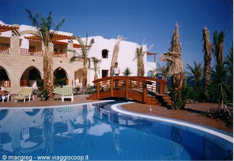 Man on wooden bridge over the pool, palms and white hotel under the sun