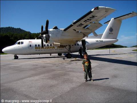Smiling child standing in front of a parked Berjaya Air twin-prop plane