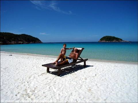 Boy and man on wooden sun lounger, white sand beach and turquoise sea