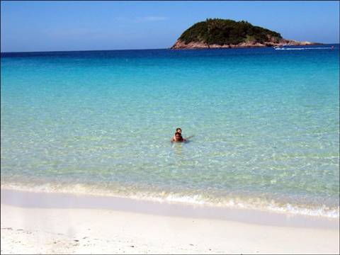 Woman swimming in turquoise water by a white sand beach and green islet