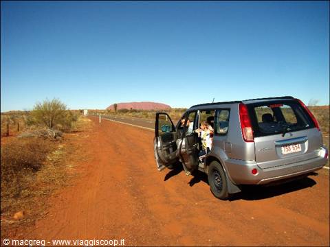 Silver car with open doors on red road, Uluru in the background