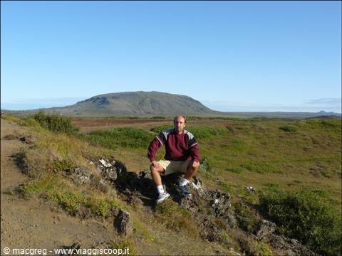 Man sitting on lava rocks among moss, flat-crater volcano in the background