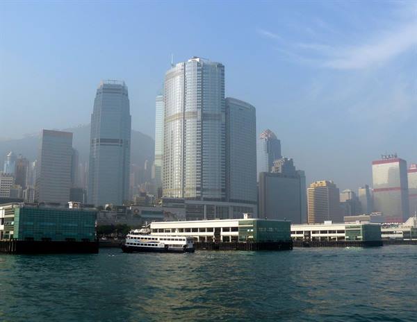 White ferry docked at green piers, glass skyscrapers over Hong Kong harbour