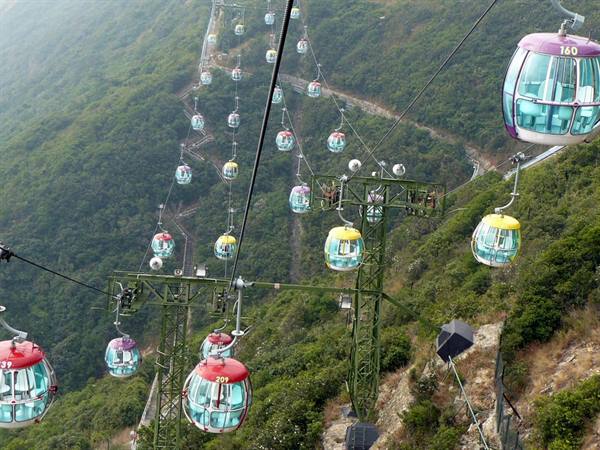 Colorful cable cars suspended over green hills, soft daylight