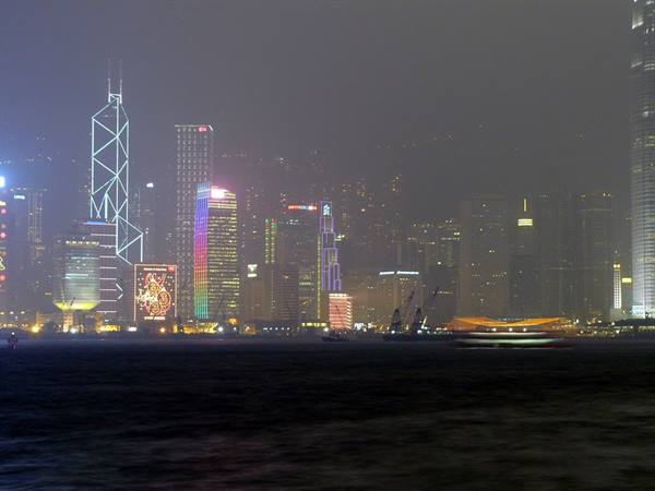 Illuminated skyscrapers across the misty bay at night, boat passing by