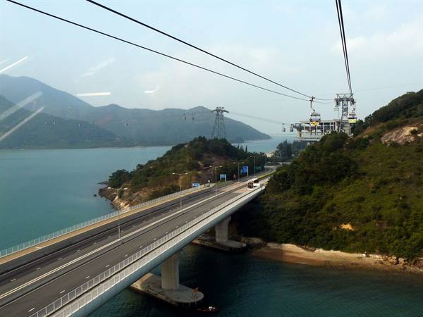 Cable cars above a highway bridge between bay and green hills, hazy daylight