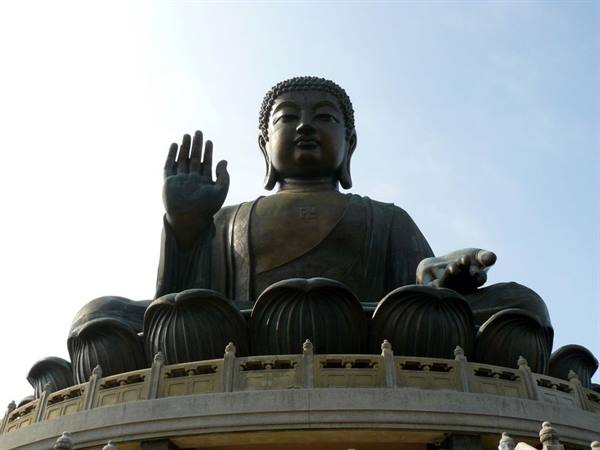 Large bronze seated Buddha statue on lotus flowers under blue sky
