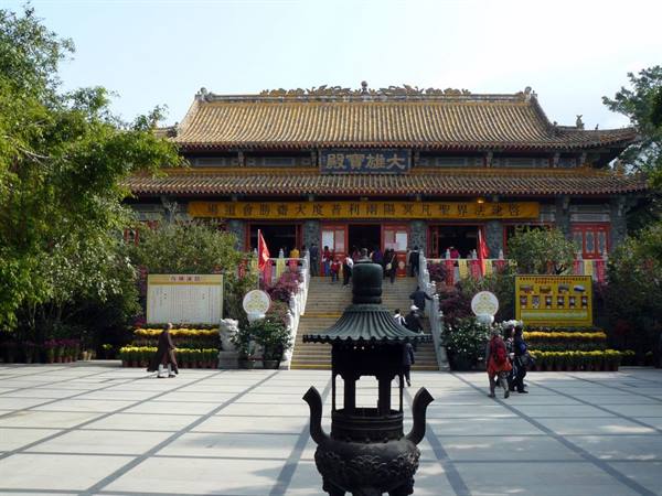 Tourists climbing the steps of a Buddhist temple with a large bronze incense burner in the foreground