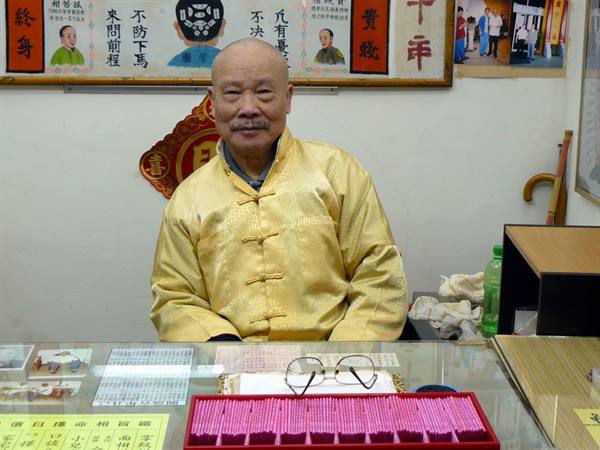 Elderly man in yellow jacket seated at a fortune-telling temple counter with divination sticks