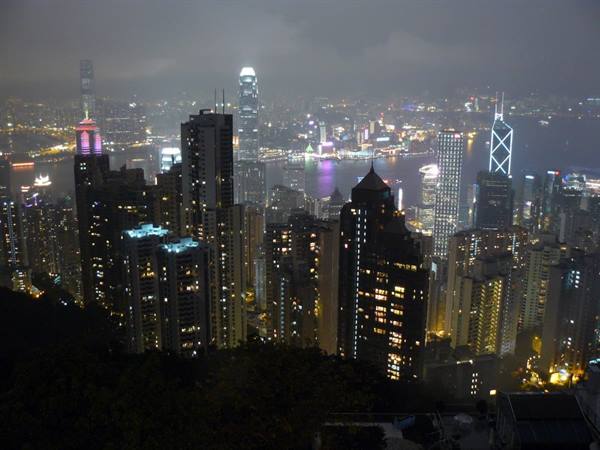 Illuminated skyscrapers at night over busy harbor, artificial lights glowing through haze