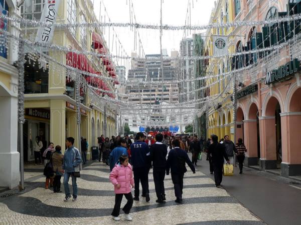 People strolling through Senado Square, wavy stone pavement, silver festive decorations overhead
