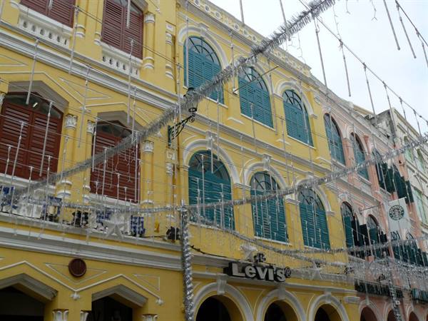 Yellow colonial building with green shutters in Macau, silver tinsel strung overhead