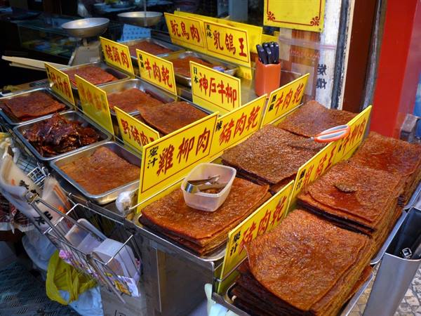 Street stall with trays of dried meat sheets and yellow signs