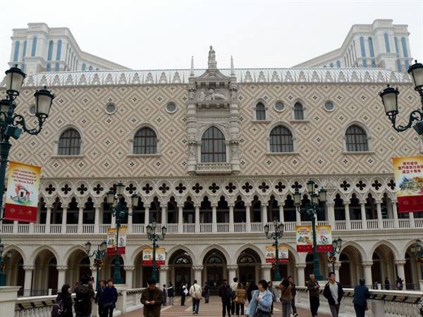 Tourists walk in front of the Venetian Macao facade with Venetian lampposts