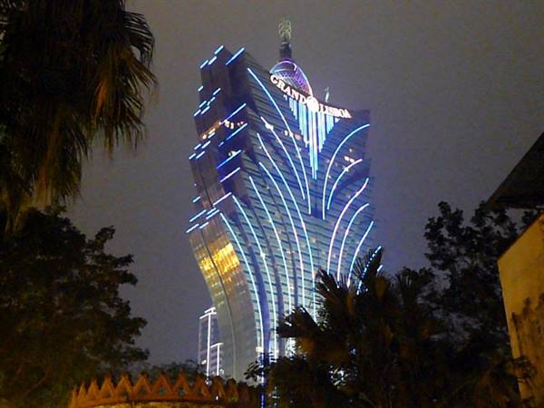The Grand Lisboa tower glowing with blue and yellow lights among palms at night